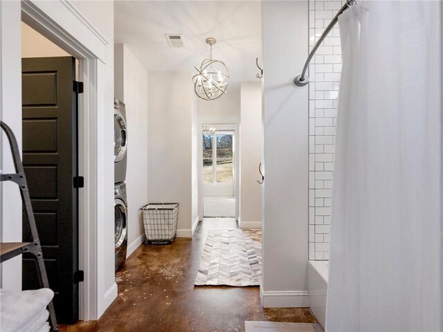 interior space with a notable chandelier, stacked washer / drying machine, visible vents, concrete flooring, and baseboards