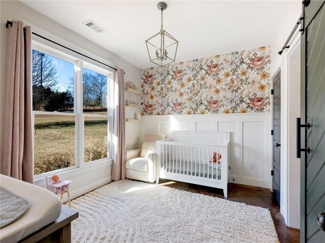 bedroom with a notable chandelier, visible vents, a barn door, wainscoting, and wallpapered walls