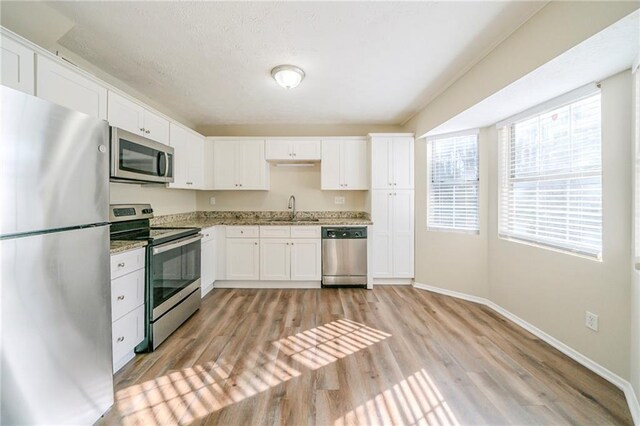 1129 Winston Dr, Decatur, GA 30032 - kitchen featuring white cabinets, appliances with stainless steel finishes, light hardwood / wood-style floors, sink, and light stone counters