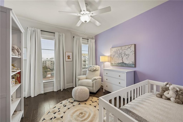 bedroom featuring a crib, dark wood finished floors, and a ceiling fan