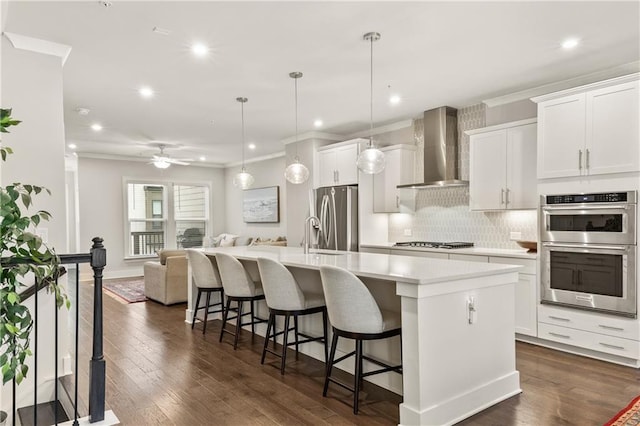 kitchen featuring open floor plan, hanging light fixtures, a kitchen island with sink, light countertops, and wall chimney range hood