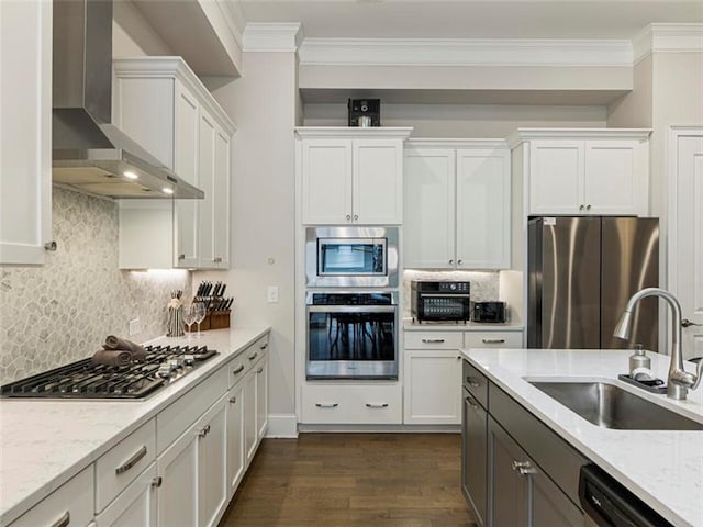 kitchen featuring tasteful backsplash, appliances with stainless steel finishes, white cabinets, wall chimney range hood, and sink