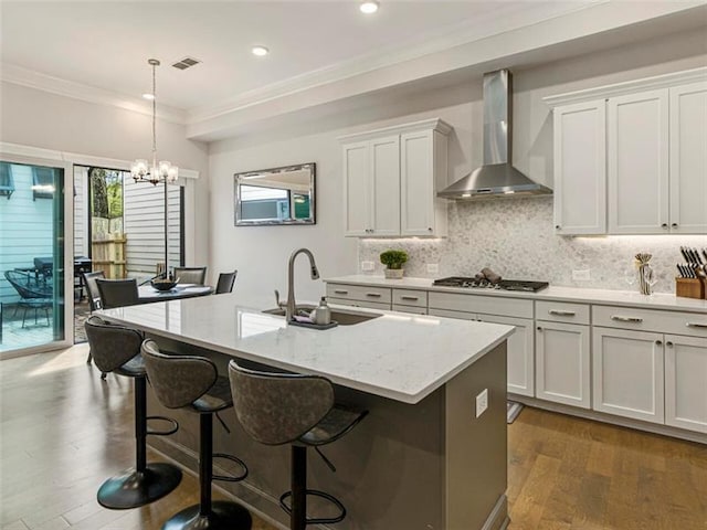 kitchen with sink, white cabinets, an island with sink, light stone countertops, and wall chimney range hood