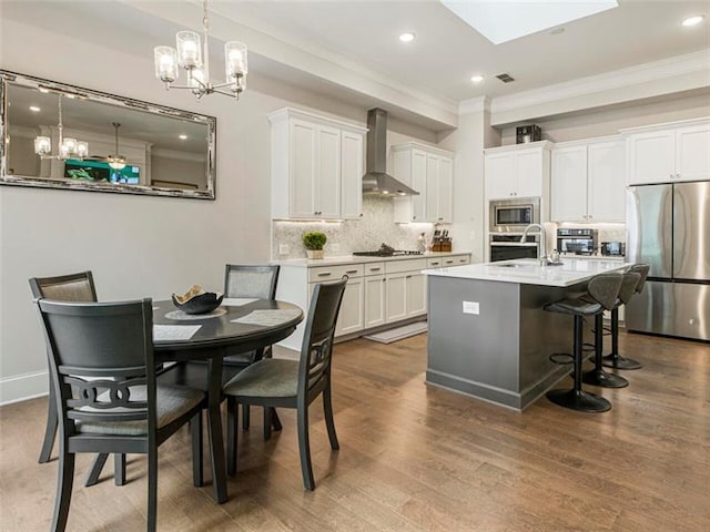 kitchen with white cabinets, appliances with stainless steel finishes, wall chimney exhaust hood, and a skylight