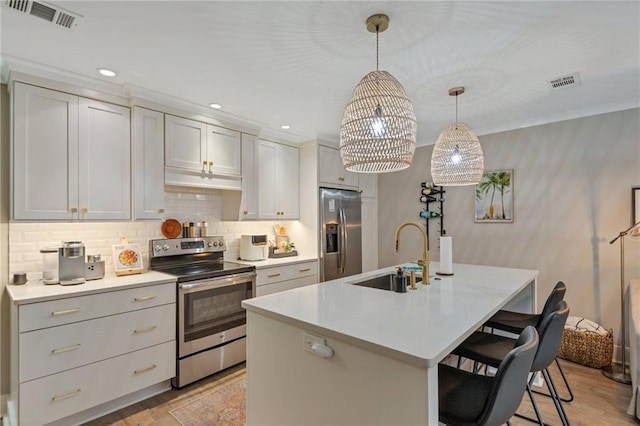 kitchen featuring sink, a breakfast bar area, appliances with stainless steel finishes, hanging light fixtures, and an island with sink