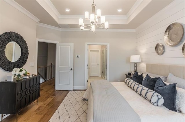 bedroom with ornamental molding, a raised ceiling, wood-type flooring, and an inviting chandelier