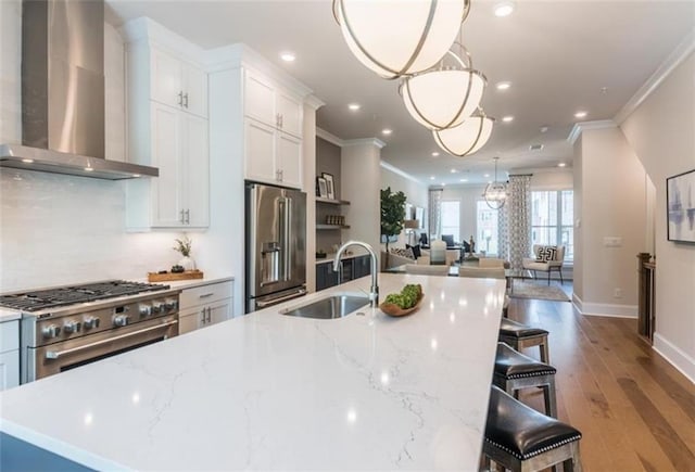 kitchen featuring light wood-type flooring, sink, hanging light fixtures, wall chimney exhaust hood, and premium appliances