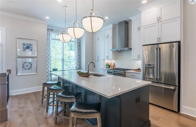 kitchen featuring an island with sink, stainless steel appliances, sink, white cabinetry, and wall chimney range hood