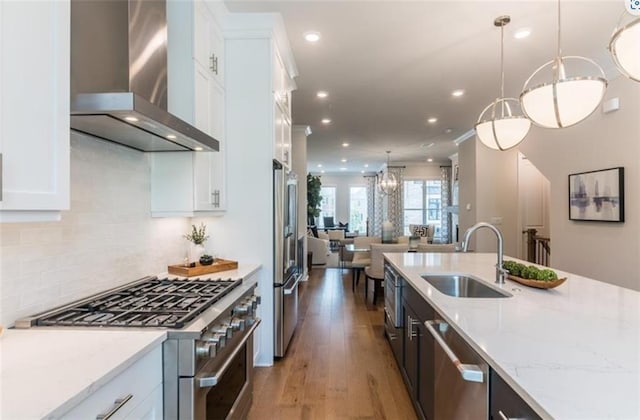 kitchen featuring wall chimney exhaust hood, white cabinetry, stainless steel appliances, and pendant lighting