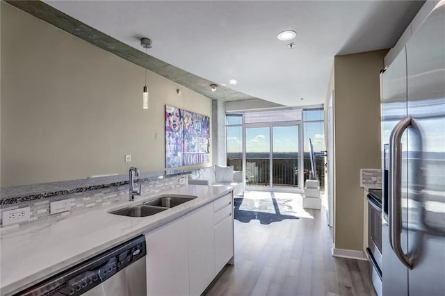 kitchen with appliances with stainless steel finishes, a sink, white cabinetry, dark wood finished floors, and pendant lighting