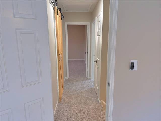 hall with a barn door and light colored carpet