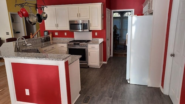 kitchen with kitchen peninsula, appliances with stainless steel finishes, dark hardwood / wood-style flooring, sink, and white cabinetry