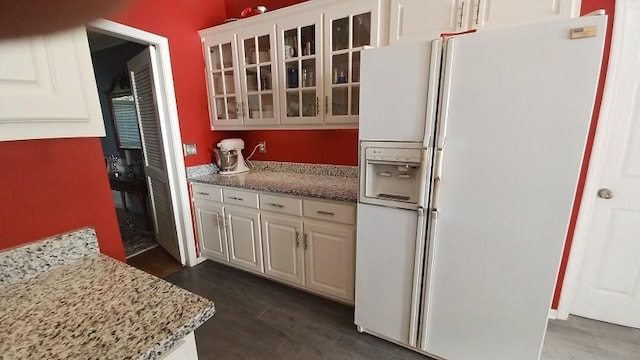 kitchen featuring light stone countertops, dark hardwood / wood-style flooring, white cabinetry, and white fridge with ice dispenser