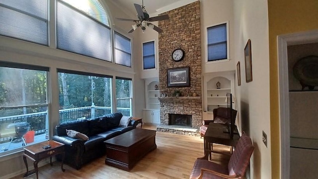 living room with ceiling fan, a high ceiling, built in features, light hardwood / wood-style floors, and a fireplace