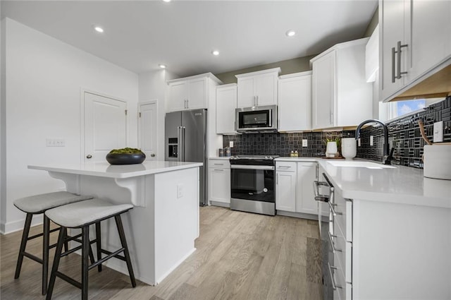 kitchen with a kitchen bar, stainless steel appliances, sink, white cabinets, and a center island