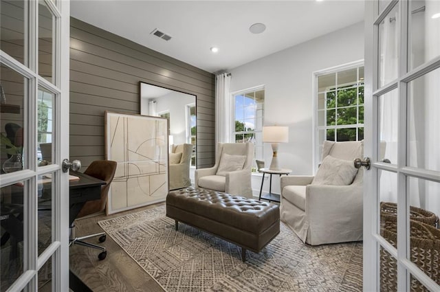 sitting room featuring hardwood / wood-style flooring, wood walls, and french doors