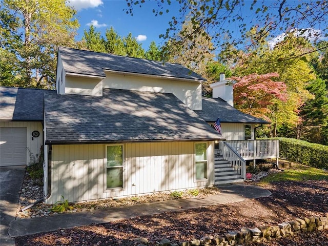 rear view of property featuring roof with shingles, a chimney, a deck, a garage, and stairs