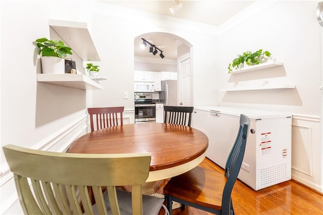 dining space with arched walkways, rail lighting, light wood-type flooring, and crown molding