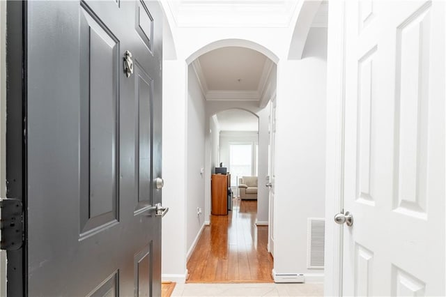 hallway with light tile patterned flooring, visible vents, crown molding, and arched walkways