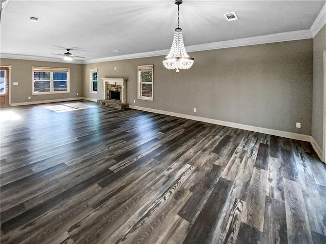 unfurnished living room with ceiling fan with notable chandelier, crown molding, dark wood-type flooring, and a stone fireplace