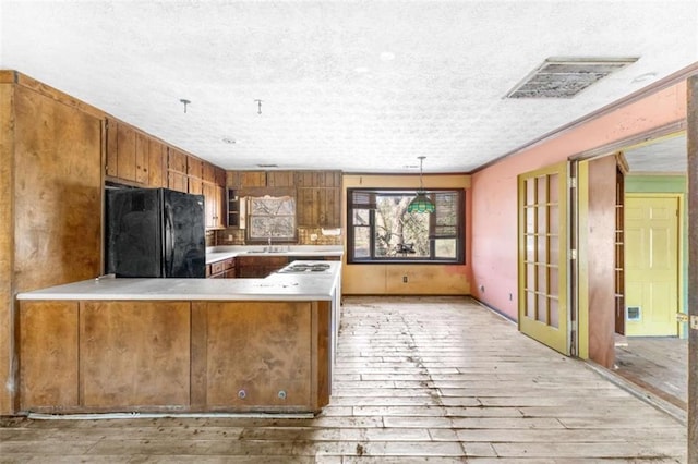 kitchen featuring light wood-type flooring, pendant lighting, sink, black fridge, and kitchen peninsula