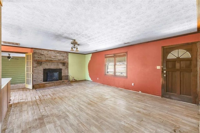 unfurnished living room with a brick fireplace, light wood-type flooring, crown molding, and a textured ceiling