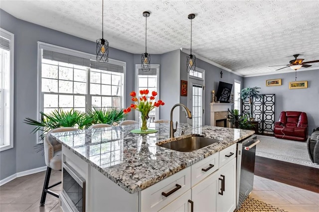 kitchen with a kitchen island with sink, a sink, white cabinetry, open floor plan, and stainless steel dishwasher