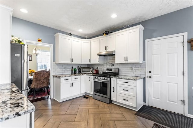 kitchen with appliances with stainless steel finishes, decorative backsplash, white cabinets, and under cabinet range hood