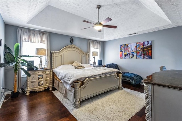 bedroom with dark wood-style floors, a tray ceiling, visible vents, and a textured ceiling