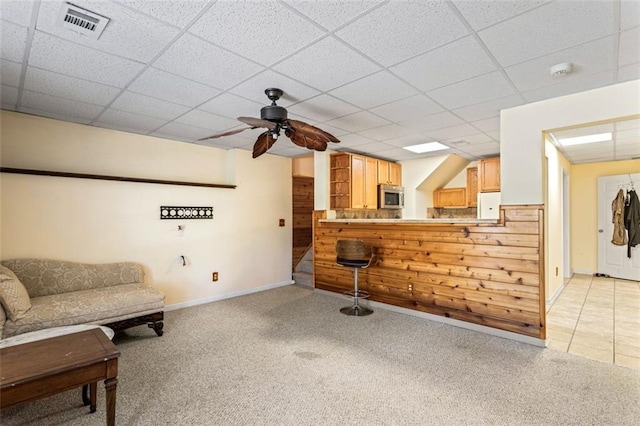 living area featuring light carpet, baseboards, visible vents, a ceiling fan, and a drop ceiling