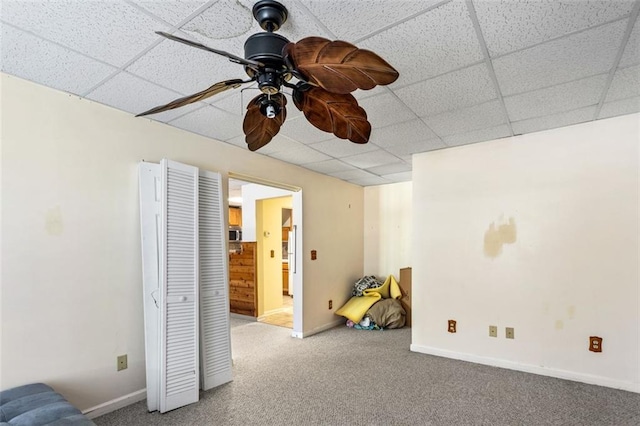 interior space with ceiling fan, baseboards, a drop ceiling, and ensuite bathroom