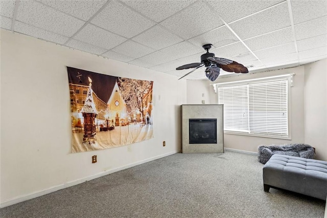 living area featuring a paneled ceiling, carpet, baseboards, and a glass covered fireplace