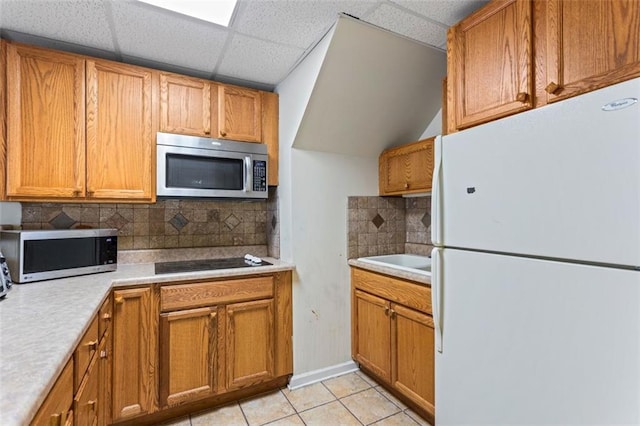 kitchen featuring freestanding refrigerator, stainless steel microwave, light tile patterned flooring, and black electric cooktop