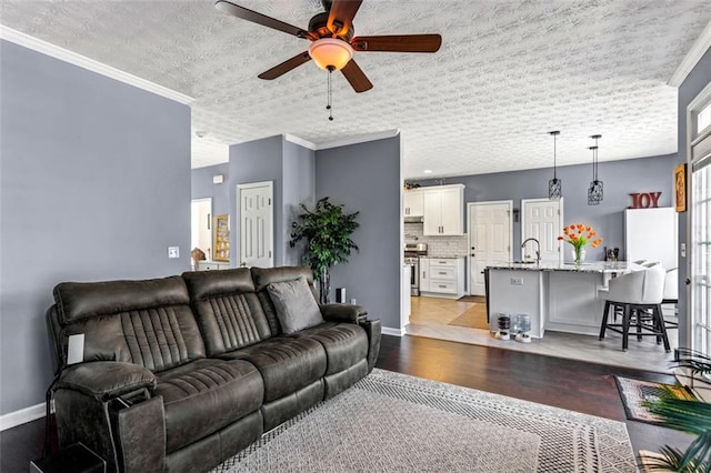 living area with baseboards, a ceiling fan, a textured ceiling, crown molding, and light wood-style floors