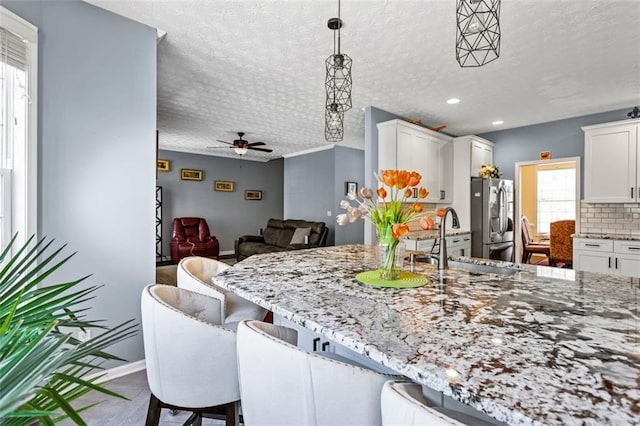 kitchen featuring a textured ceiling, a breakfast bar, a sink, stainless steel refrigerator with ice dispenser, and light stone countertops