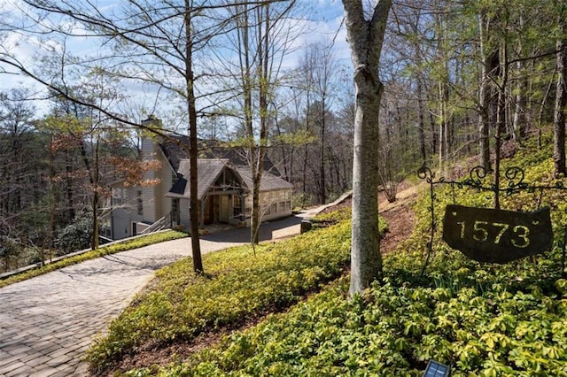 surrounding community with decorative driveway and a wooded view