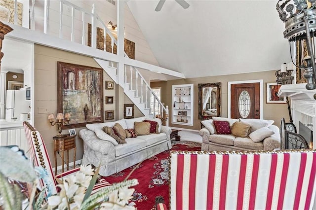 living area with carpet, a fireplace, a ceiling fan, high vaulted ceiling, and stairs