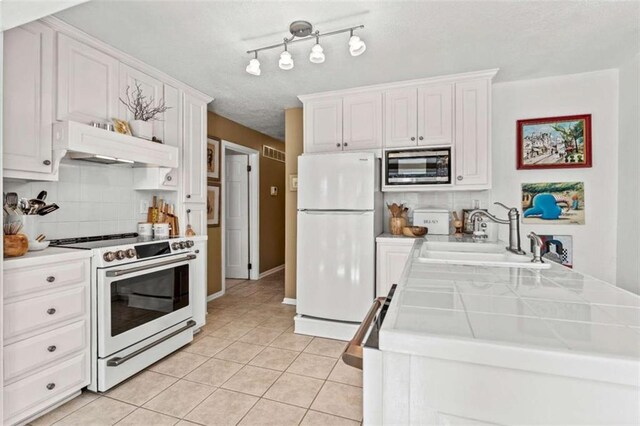 kitchen with light tile patterned flooring, under cabinet range hood, a peninsula, a sink, and appliances with stainless steel finishes