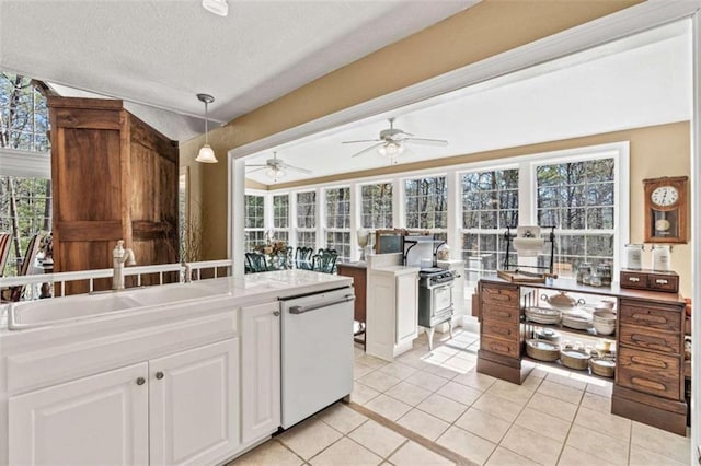 kitchen featuring light tile patterned floors, plenty of natural light, white dishwasher, white cabinetry, and a sink