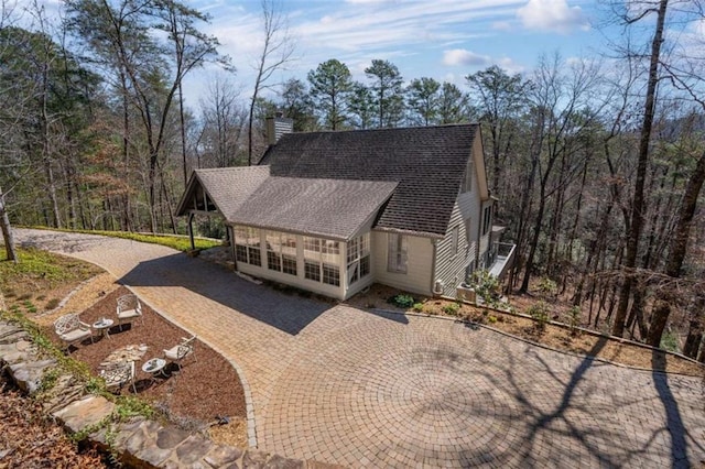 view of front of property featuring roof with shingles, driveway, a chimney, and a wooded view