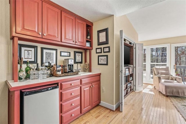 bar featuring a dry bar, light wood finished floors, lofted ceiling, freestanding refrigerator, and a sink