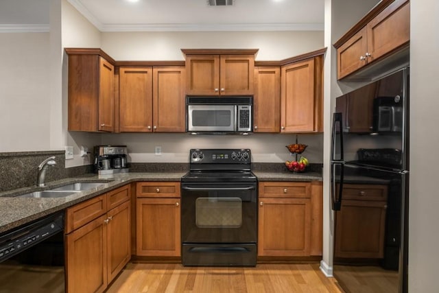 kitchen featuring a sink, black appliances, light wood finished floors, brown cabinetry, and crown molding