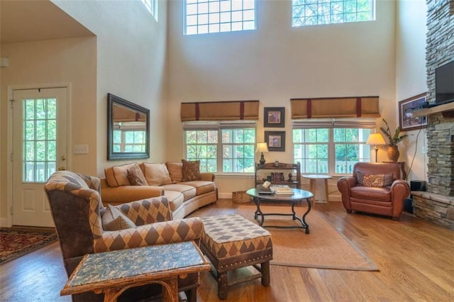 living room with a stone fireplace, hardwood / wood-style floors, a healthy amount of sunlight, and a high ceiling