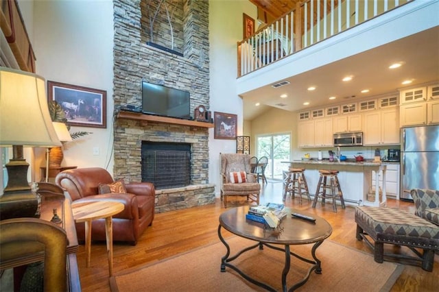 living room with a fireplace, high vaulted ceiling, and light hardwood / wood-style flooring