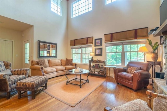 living room with light wood-type flooring, a towering ceiling, and a fireplace