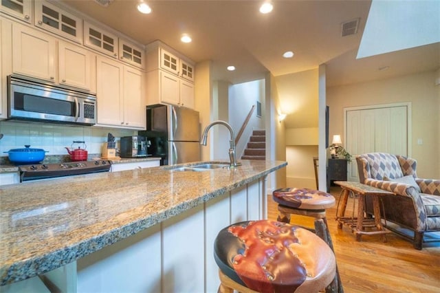 kitchen with light stone countertops, backsplash, stainless steel appliances, sink, and light hardwood / wood-style flooring