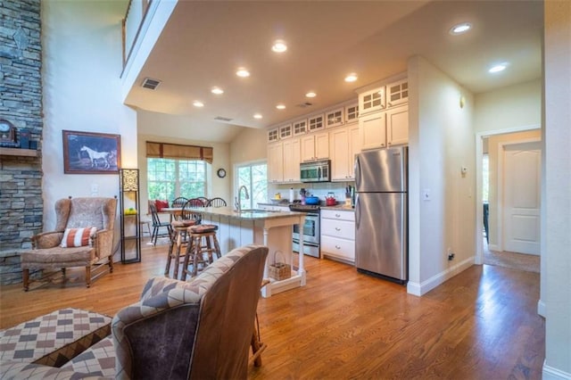 kitchen featuring white cabinets, an island with sink, appliances with stainless steel finishes, light hardwood / wood-style floors, and a kitchen bar