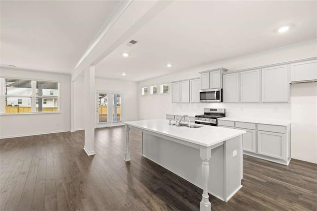 kitchen with stainless steel appliances, dark wood-type flooring, a sink, light countertops, and an island with sink