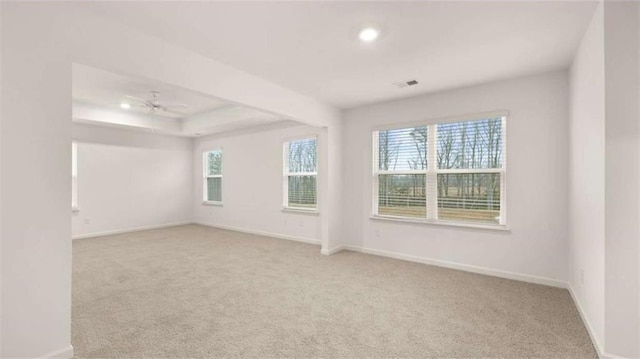 empty room with visible vents, baseboards, a raised ceiling, light colored carpet, and ceiling fan