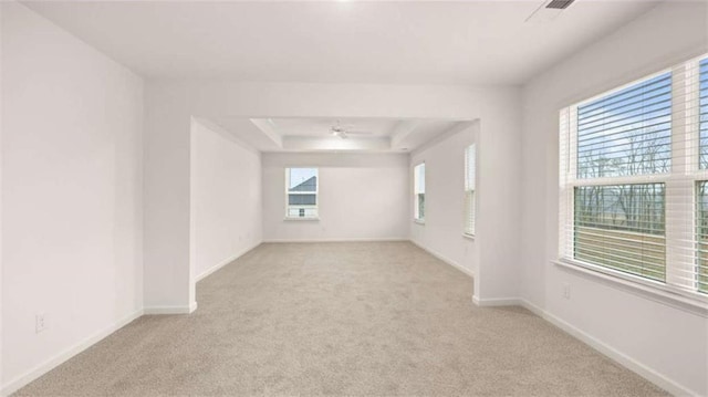 spare room featuring light carpet, baseboards, a tray ceiling, and a ceiling fan